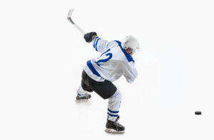 Young man, hockey player in motion during game, hitting puck with stick against white studio background.